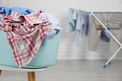 Plastic laundry basket overfilled with clothes on white stool indoors. Space for text
