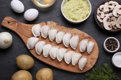 Photo of Raw dumplings (varenyky) and ingredients on black table, flat lay