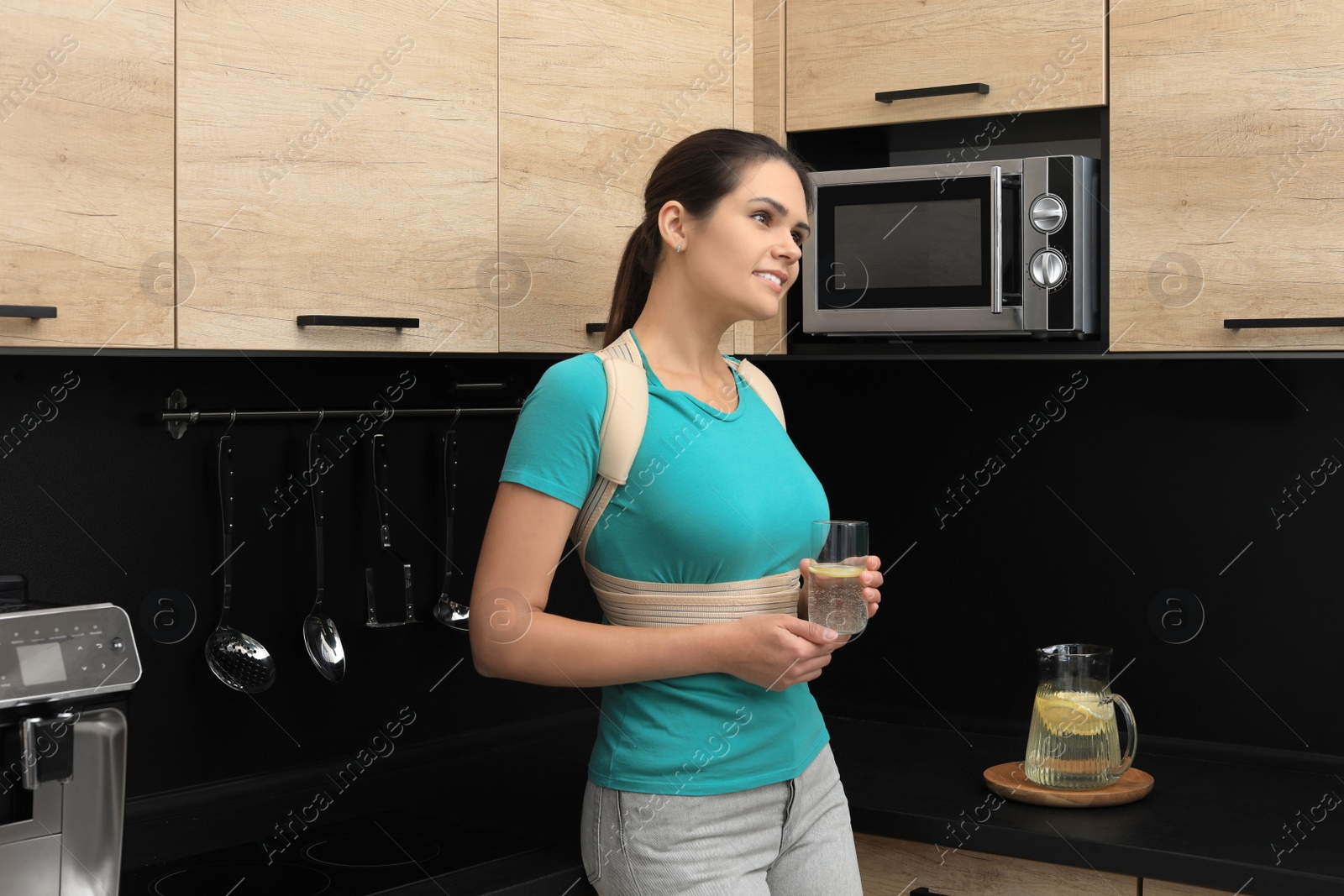 Photo of Woman with orthopedic corset holding glass of lemonade in kitchen