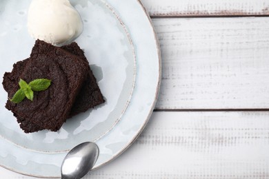 Photo of Tasty brownies served with ice cream and mint on white wooden table, top view. Space for text