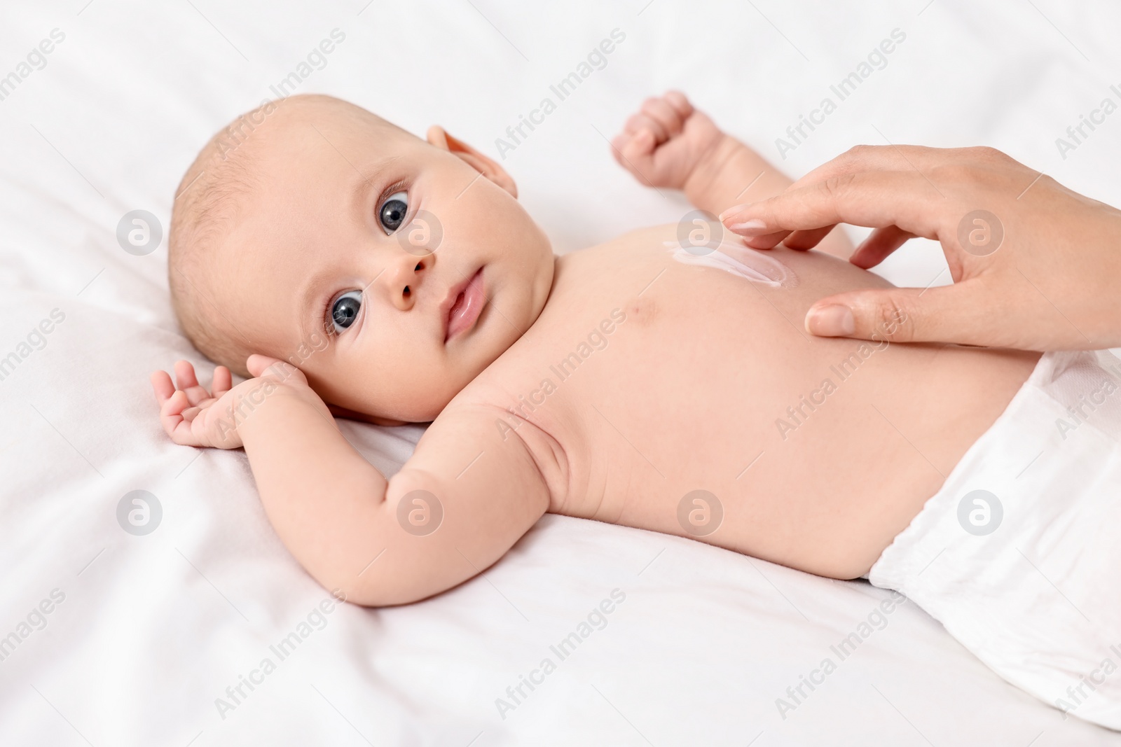 Photo of Woman applying body cream onto baby`s skin on bed, closeup