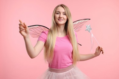 Photo of Beautiful girl in fairy costume with wings and magic wand on pink background