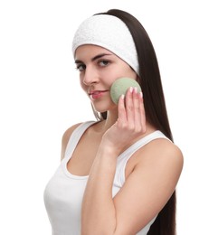 Young woman with headband washing her face using sponge on white background