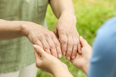 Photo of Elderly woman and female caregiver holding hands outdoors, closeup