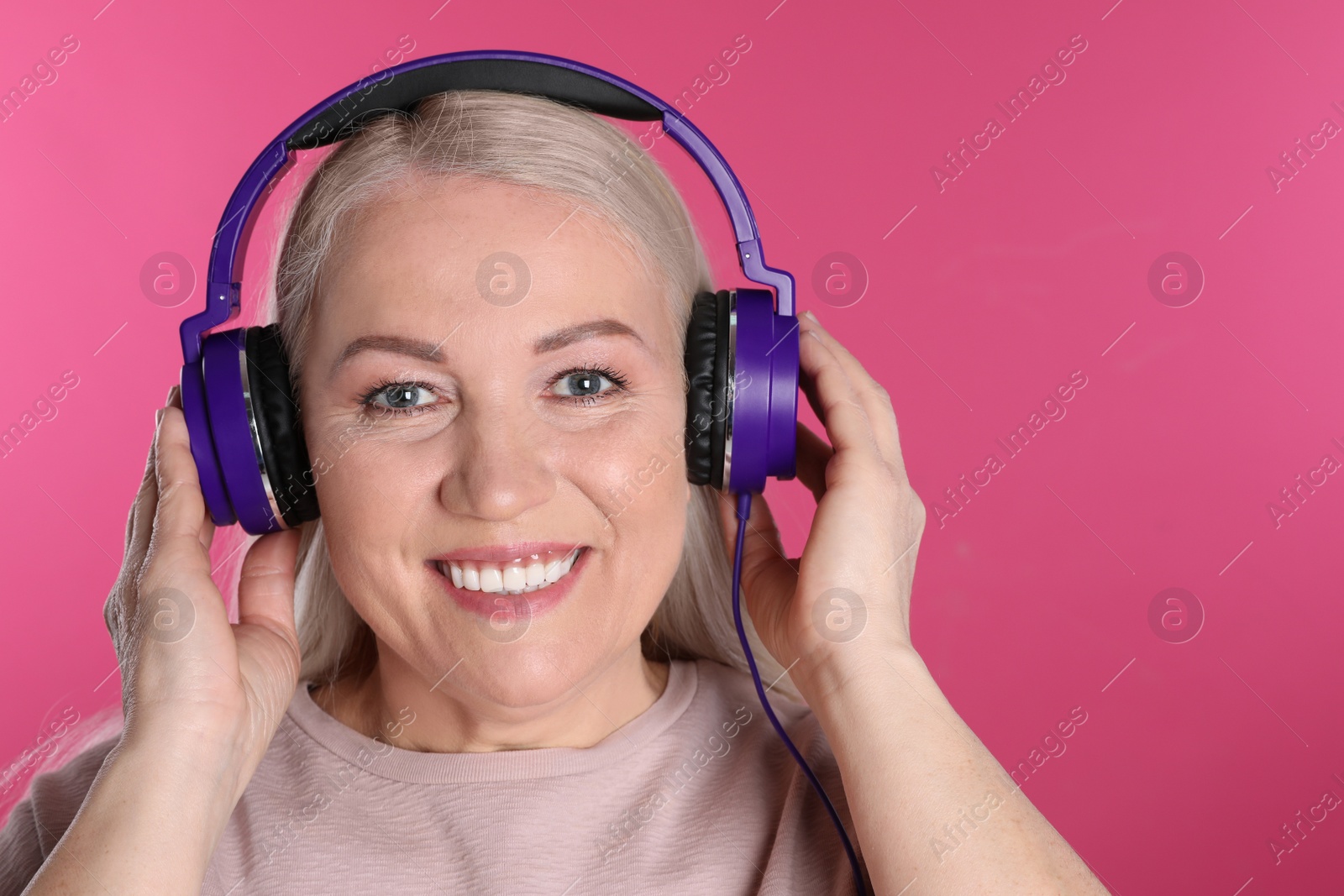 Photo of Mature woman enjoying music in headphones on color background