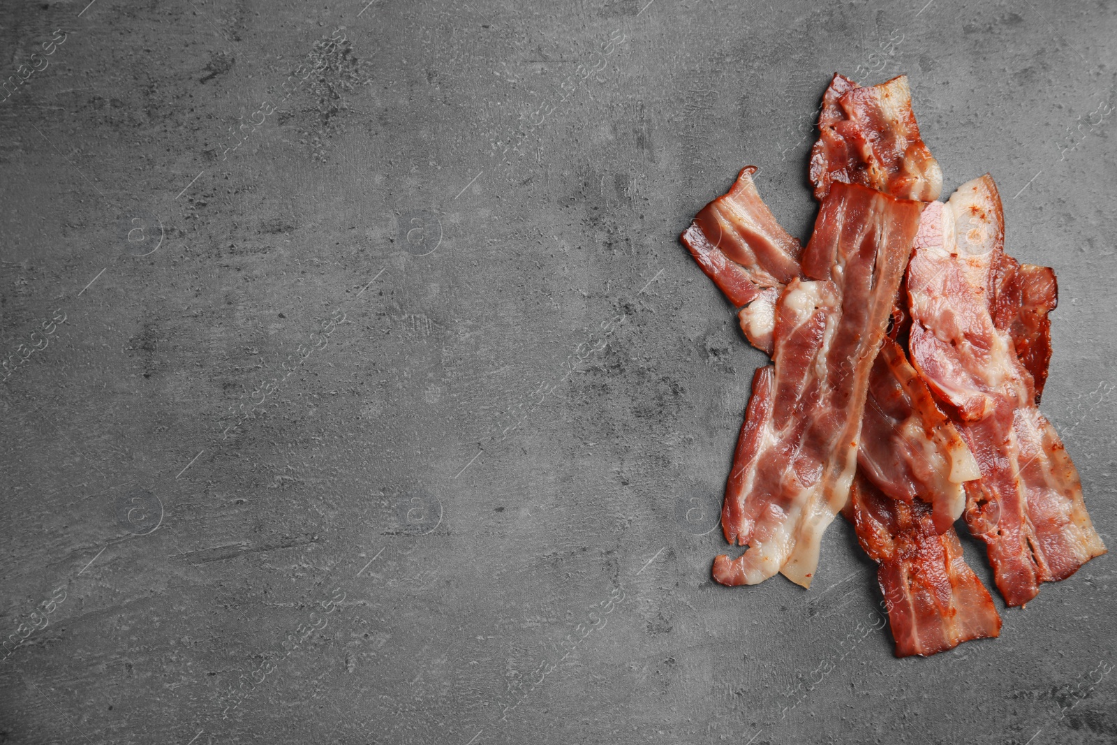 Photo of Slices of tasty fried bacon on dark background, top view. Space for text