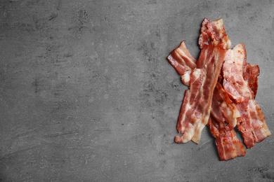 Photo of Slices of tasty fried bacon on dark background, top view. Space for text