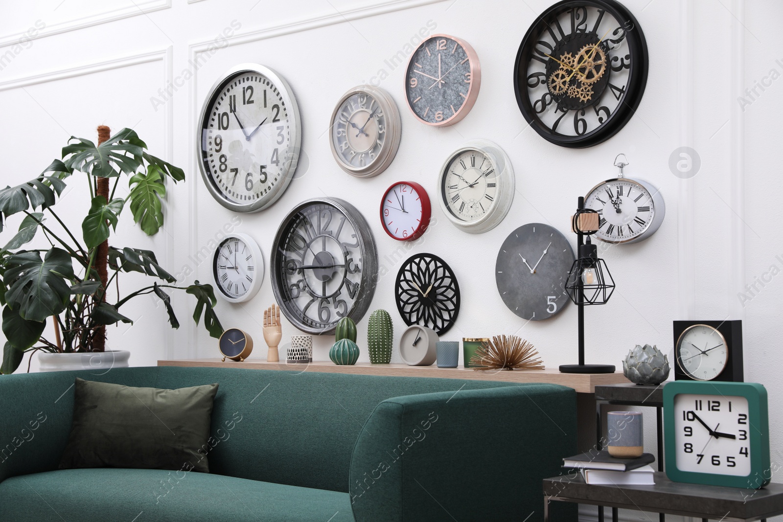 Photo of Collection of different clocks and comfortable sofa in stylish room. Interior design