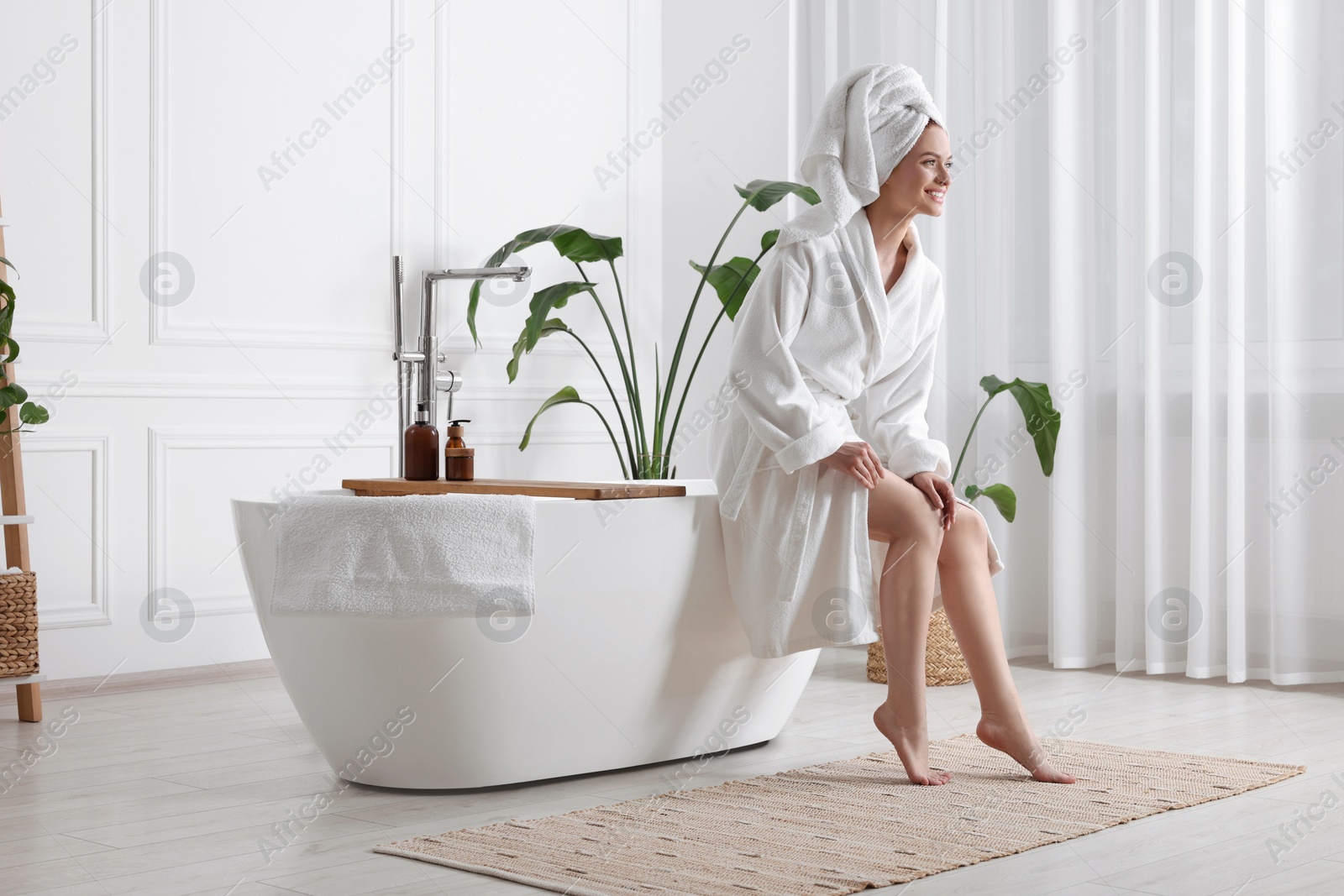 Photo of Beautiful young woman touching her smooth legs in bathroom, space for text