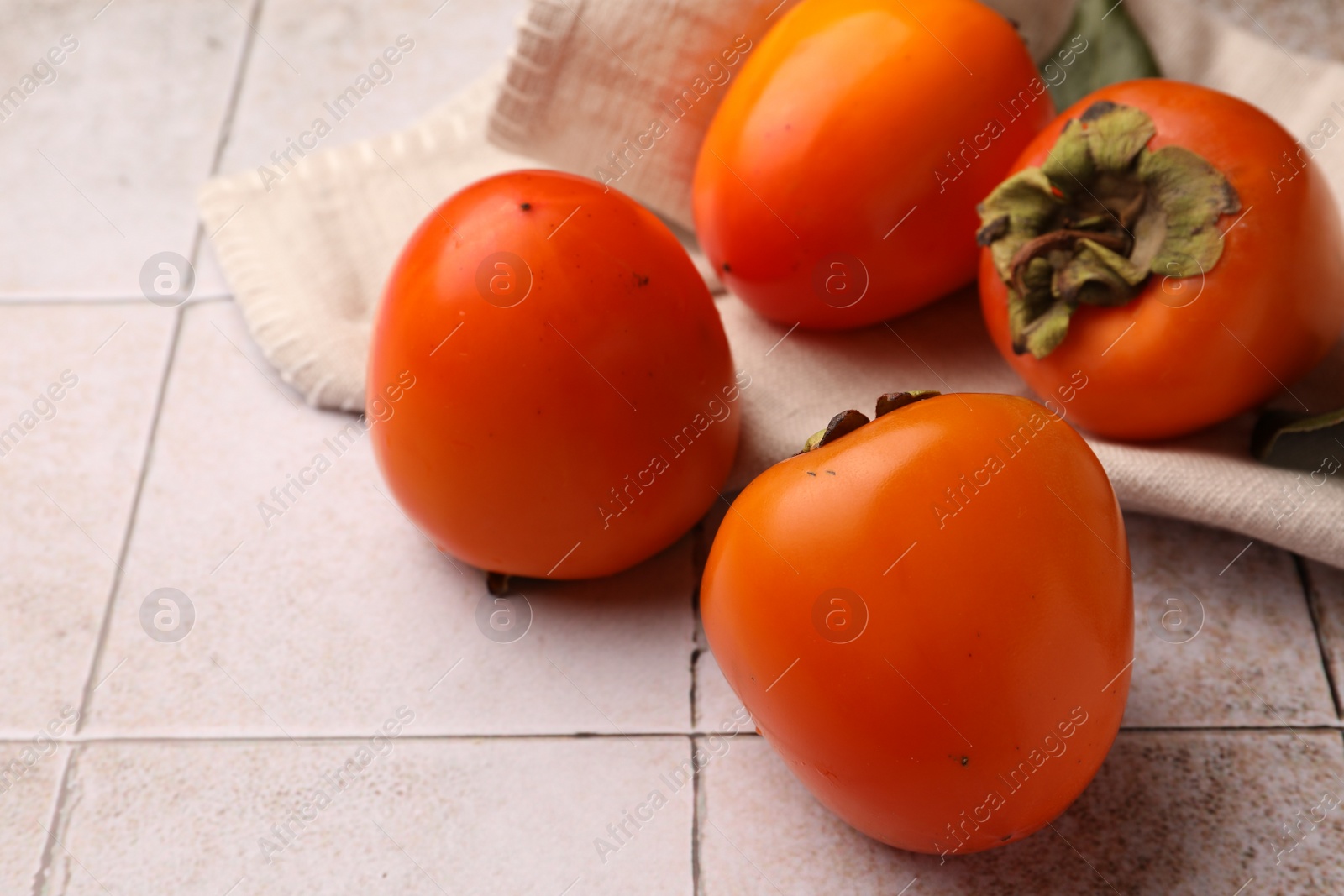 Photo of Delicious ripe juicy persimmons on tiled surface, space for text