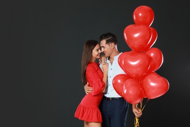 Photo of Beautiful couple with heart shaped balloons on dark background, space for text