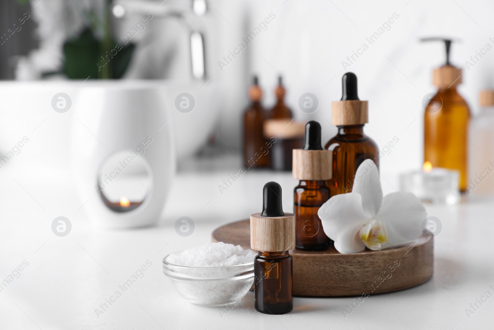 Photo of Essential oils, orchid flower and sea salt on white countertop in bathroom. Space for text