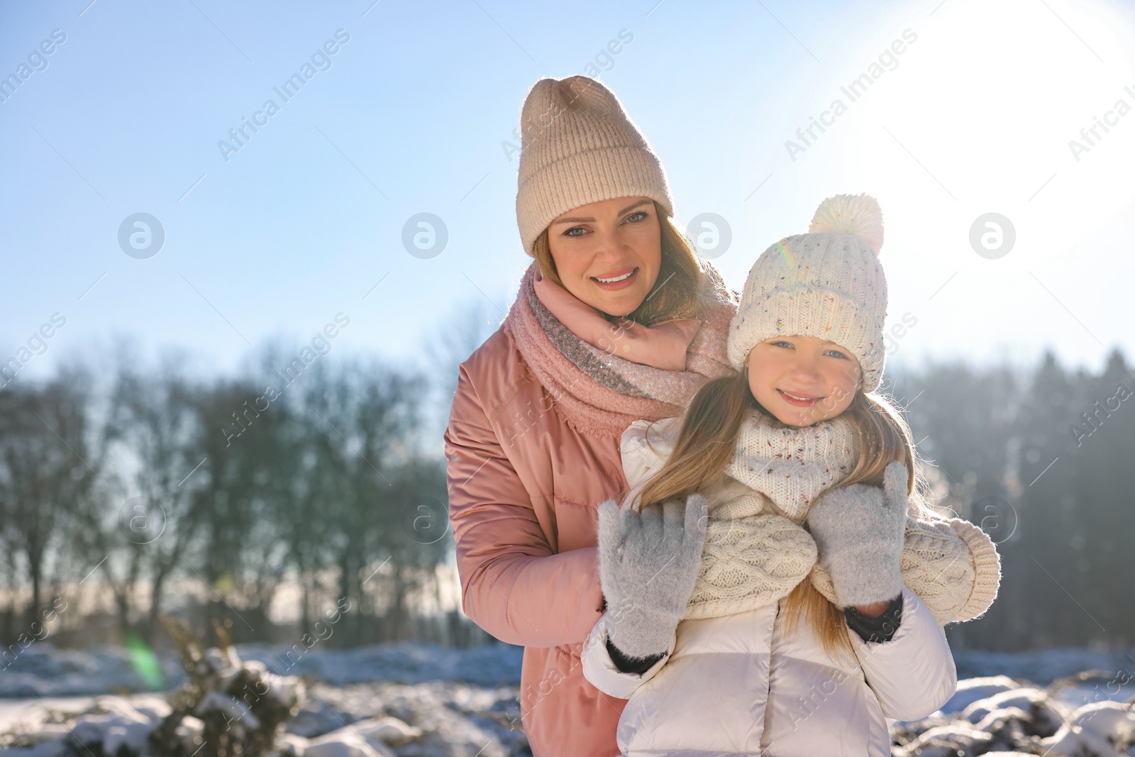 Photo of Family portrait of happy mother and her daughter in sunny snowy park. Space for text