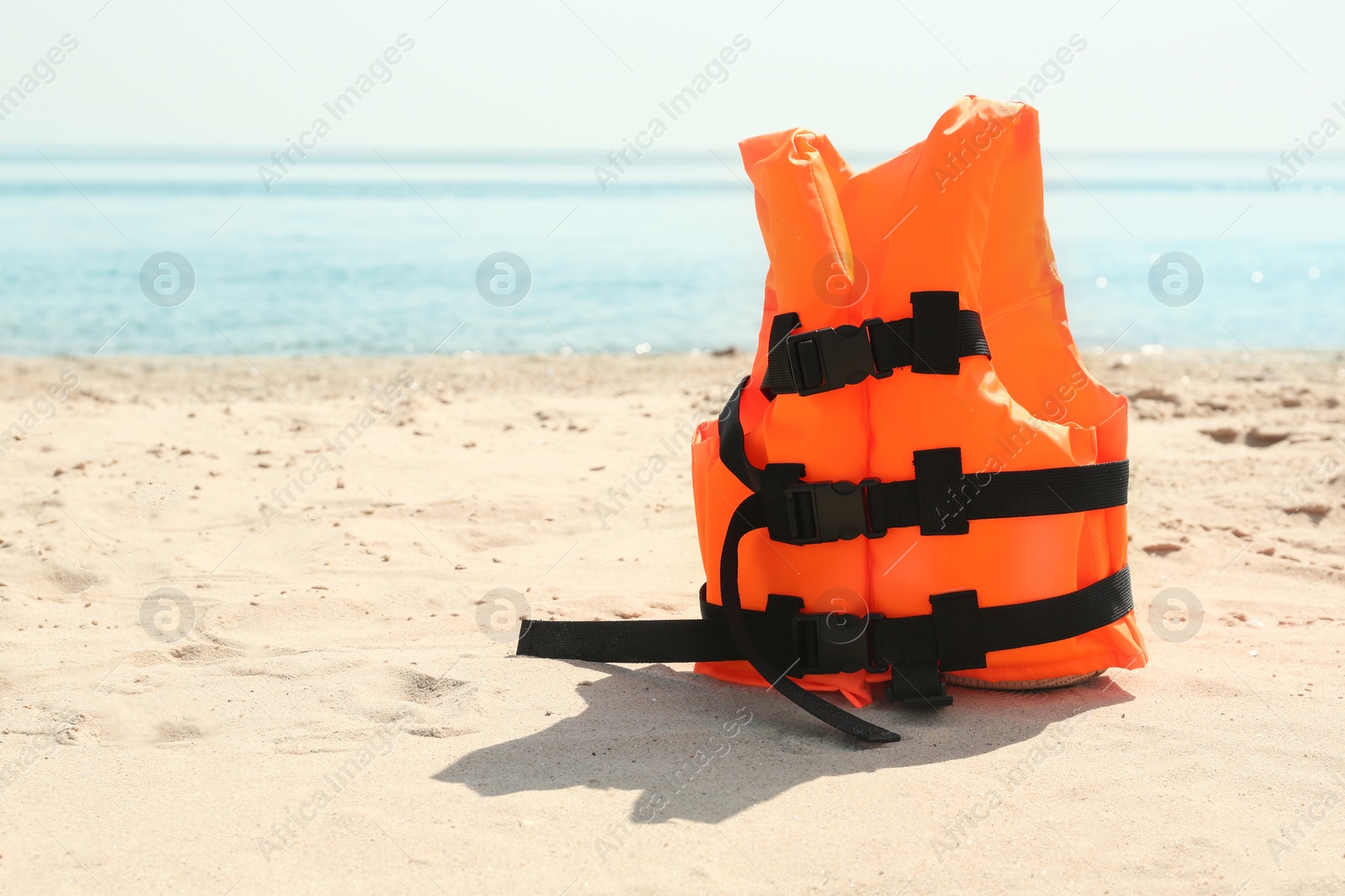 Photo of Orange life jacket on sandy beach near sea. Emergency rescue equipment