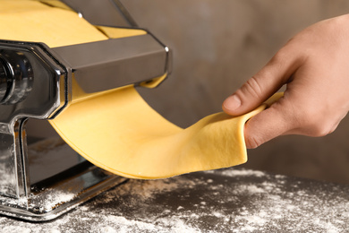 Woman preparing dough with pasta maker machine at table, closeup