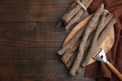 Photo of Raw salsify roots and peeler on wooden table, flat lay. Space for text