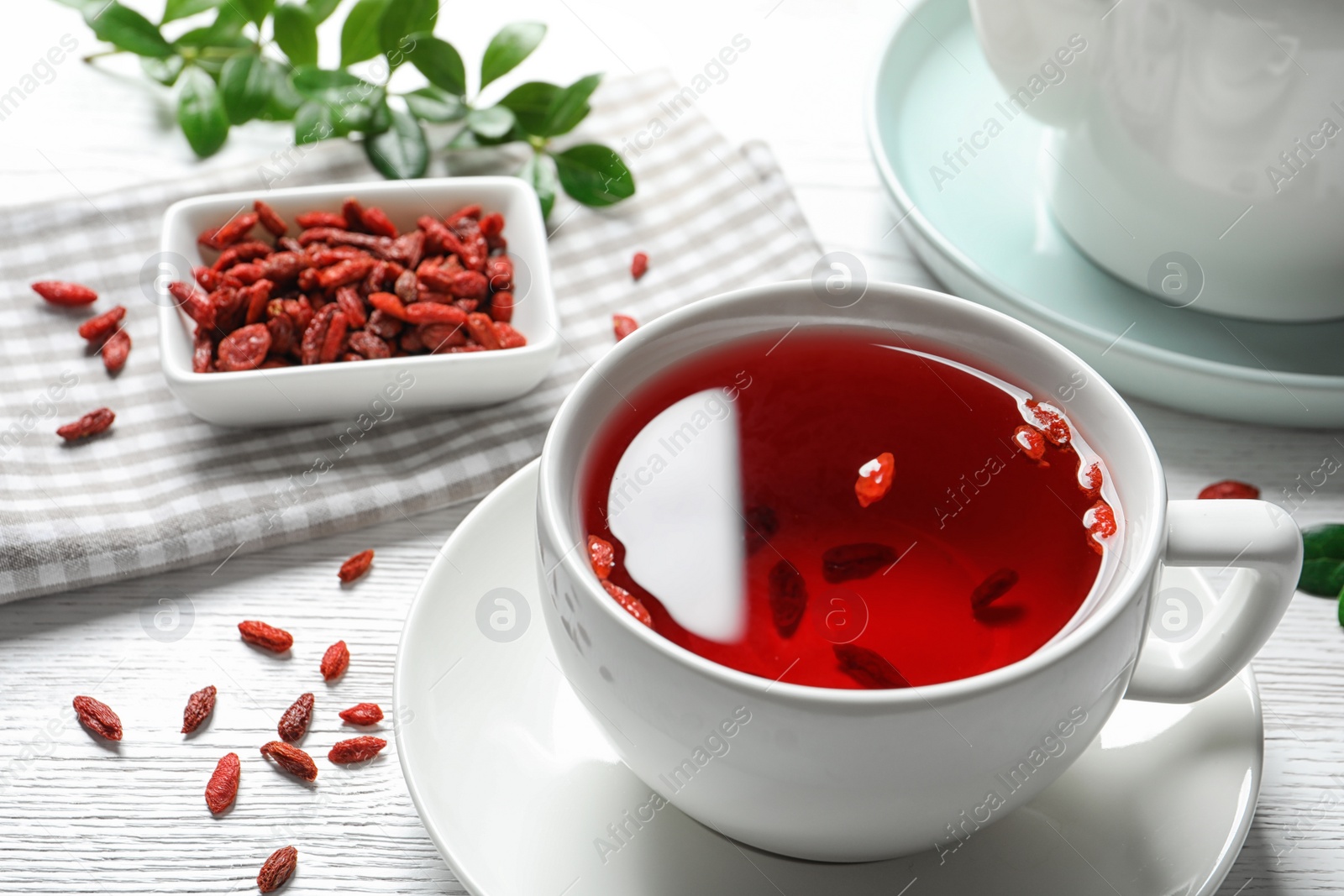 Photo of Healthy goji tea in cup on white wooden table