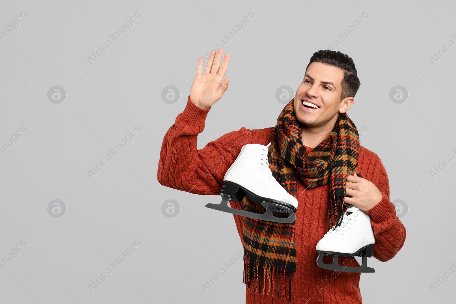 Photo of Happy man with ice skates on grey background. Space for text