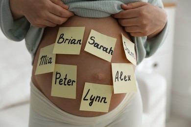 Photo of Pregnant woman with different baby names on belly indoors, closeup