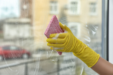 Woman cleaning window with sponge at home, closeup