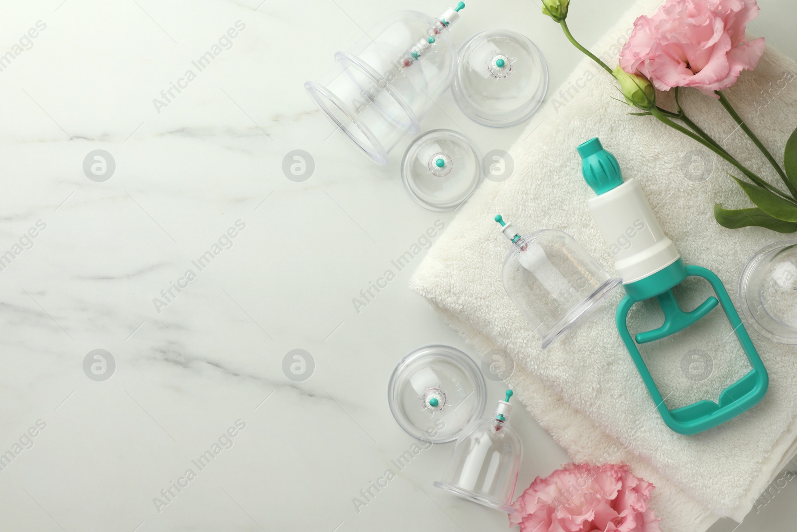 Photo of Plastic cups, hand pump, flowers and towel on white marble table, flat lay with space for text. Cupping therapy