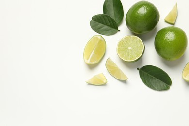 Photo of Whole and cut fresh ripe limes with green leaves on white background, flat lay