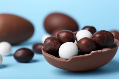 Tasty chocolate egg with different sweets inside on light blue background, closeup. Space for text