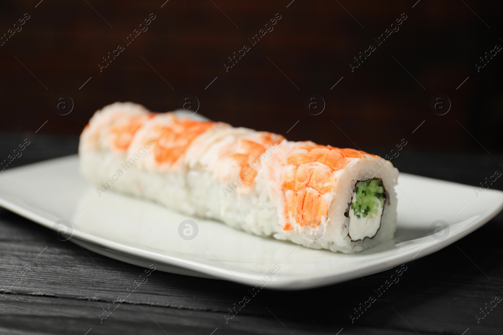 Photo of Tasty sushi rolls with shrimps, cream cheese and cucumber on black wooden table, closeup