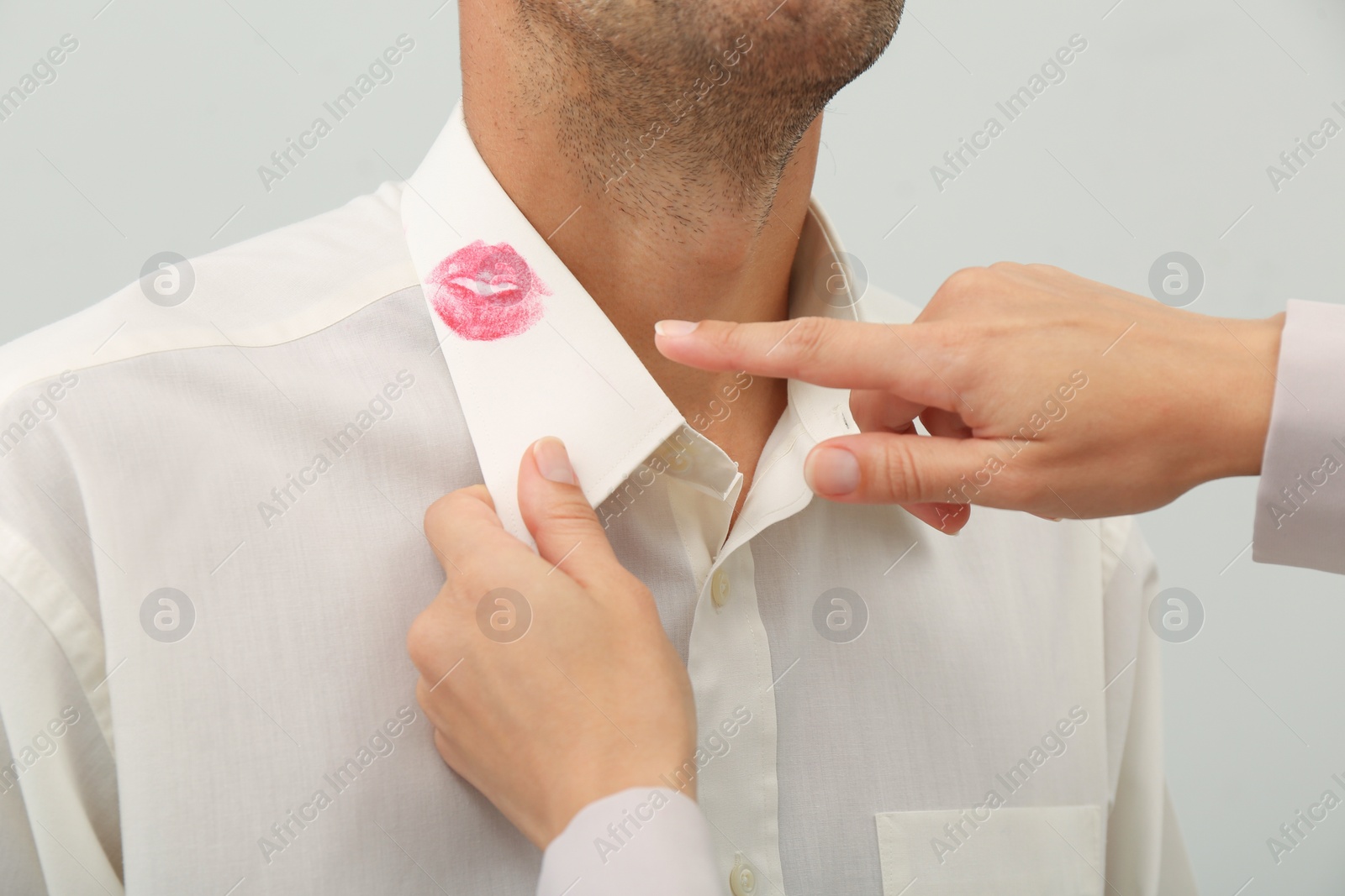 Photo of Woman pointing at lipstick kiss mark on her husband's shirt, closeup