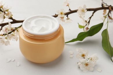 Jar of face cream, leaves, tree branch and flowers on white marble table