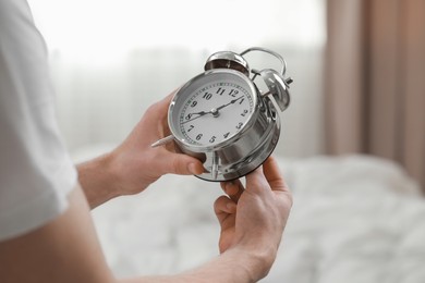 Photo of Man with alarm clock in bedroom, closeup of hands