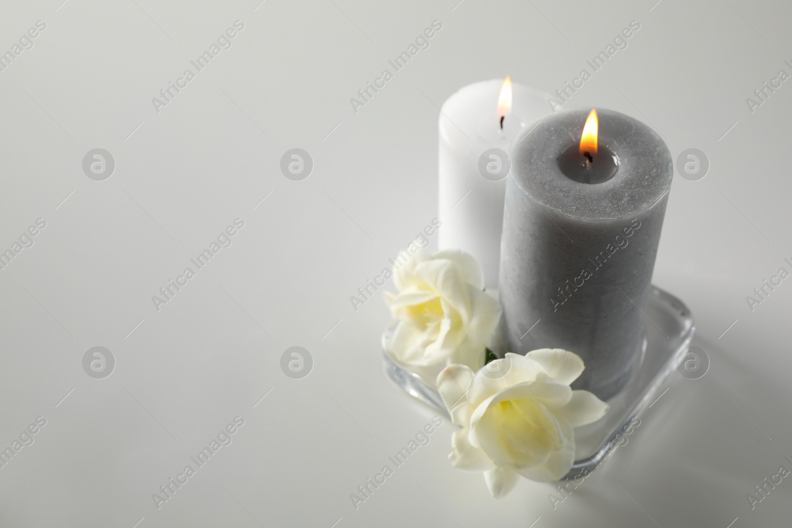 Photo of Wax candles and flowers in glass holder on white table. Space for text