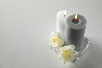 Wax candles and flowers in glass holder on white table. Space for text