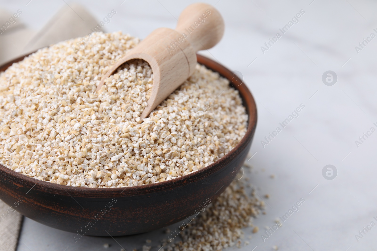 Photo of Dry barley groats and scoop in bowl on white table, closeup. Space for text