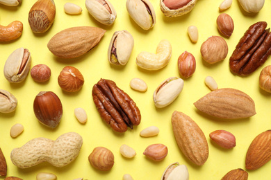 Different delicious nuts on yellow background, flat lay