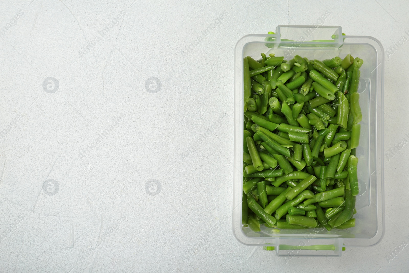 Photo of Plastic container with frozen green beans on light background, top view. Vegetable preservation