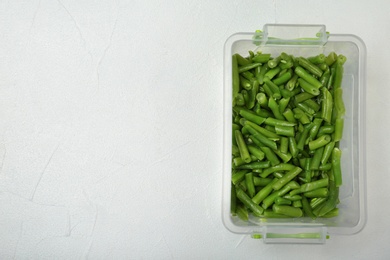 Plastic container with frozen green beans on light background, top view. Vegetable preservation