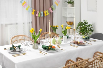 Photo of Festive Easter table setting with painted eggs, burning candles and yellow tulips in room