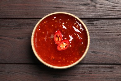 Photo of Spicy chili sauce in bowl on wooden table, top view