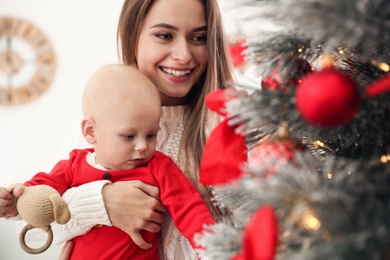 Photo of Happy mother with cute baby near Christmas tree at home