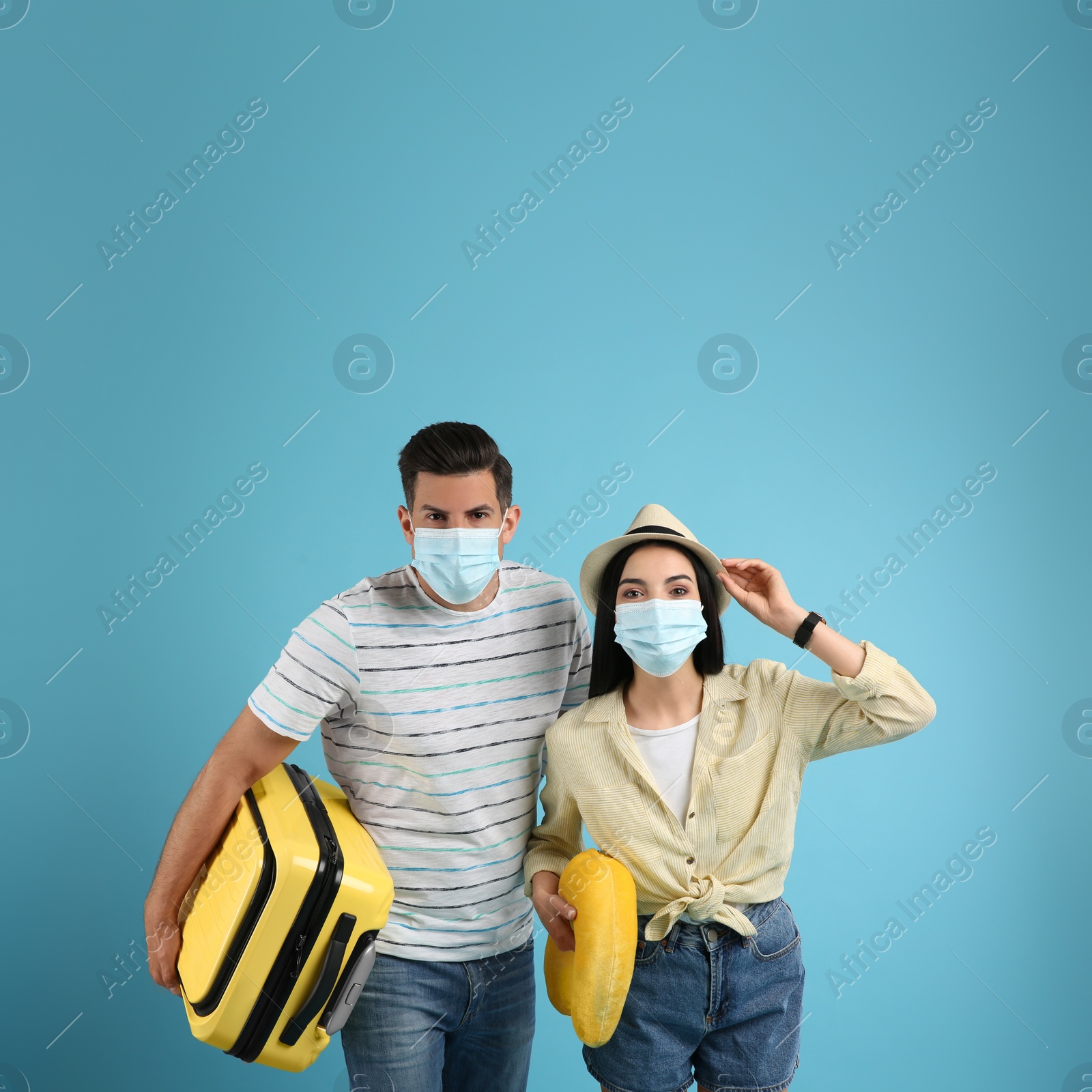 Photo of Couple of tourists in medical masks on light blue background. Travelling during coronavirus pandemic