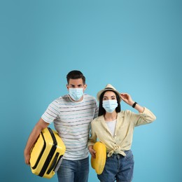 Photo of Couple of tourists in medical masks on light blue background. Travelling during coronavirus pandemic