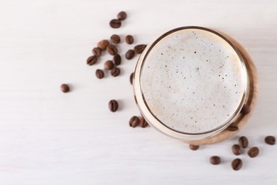 Photo of Refreshing iced coffee with milk in glass and beans on white table, top view. Space for text