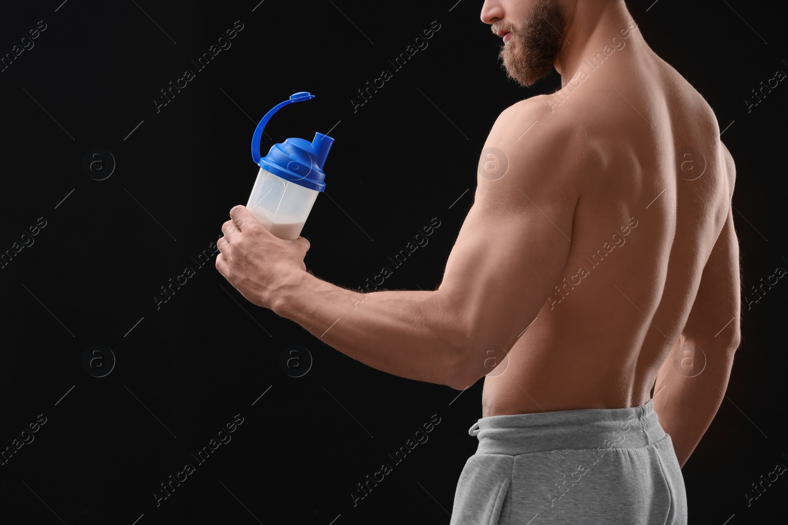 Photo of Young man with muscular body holding shaker of protein on black background, closeup