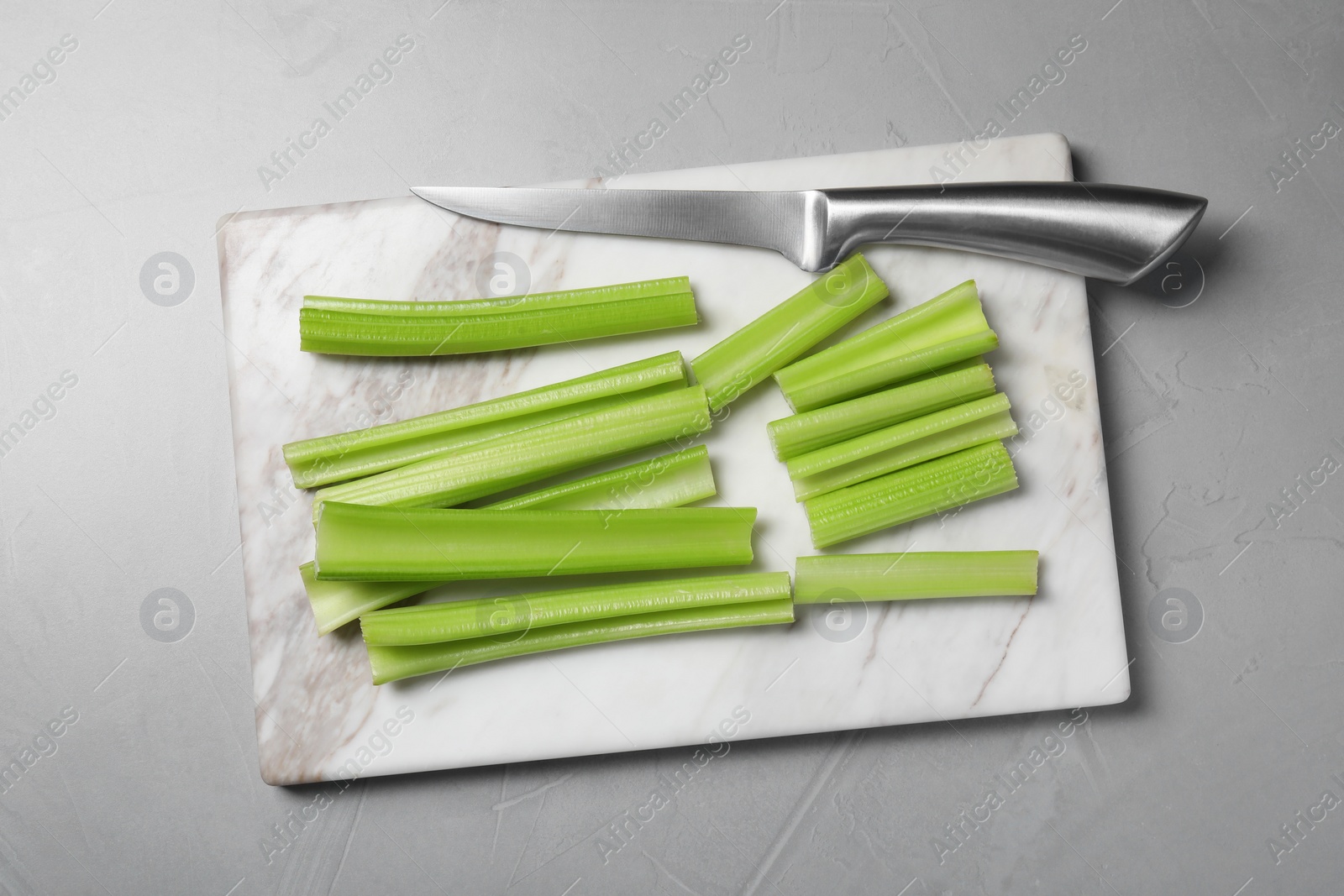 Photo of Board with fresh green cut celery and knife on light grey table, top view