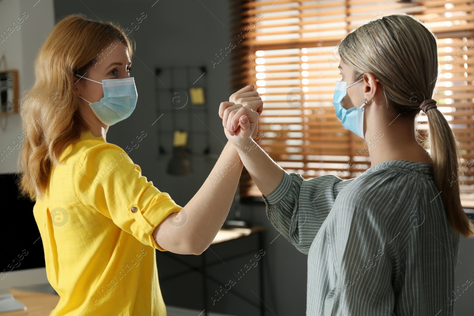 Photo of People greeting each other by bumping fists instead of handshake indoors