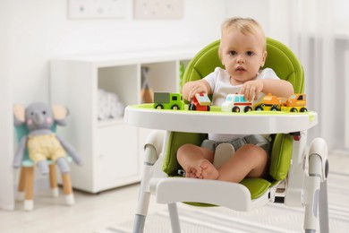 Photo of Children toys. Cute little boy playing with toy cars in high chair at home, space for text