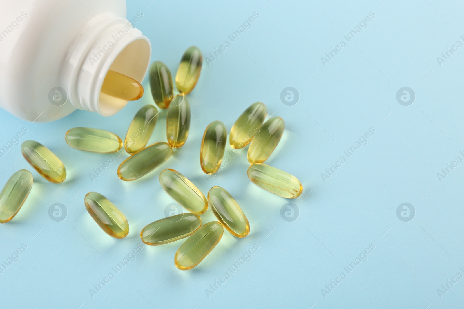 Photo of Bottle and vitamin capsules on light blue background, closeup. Space for text