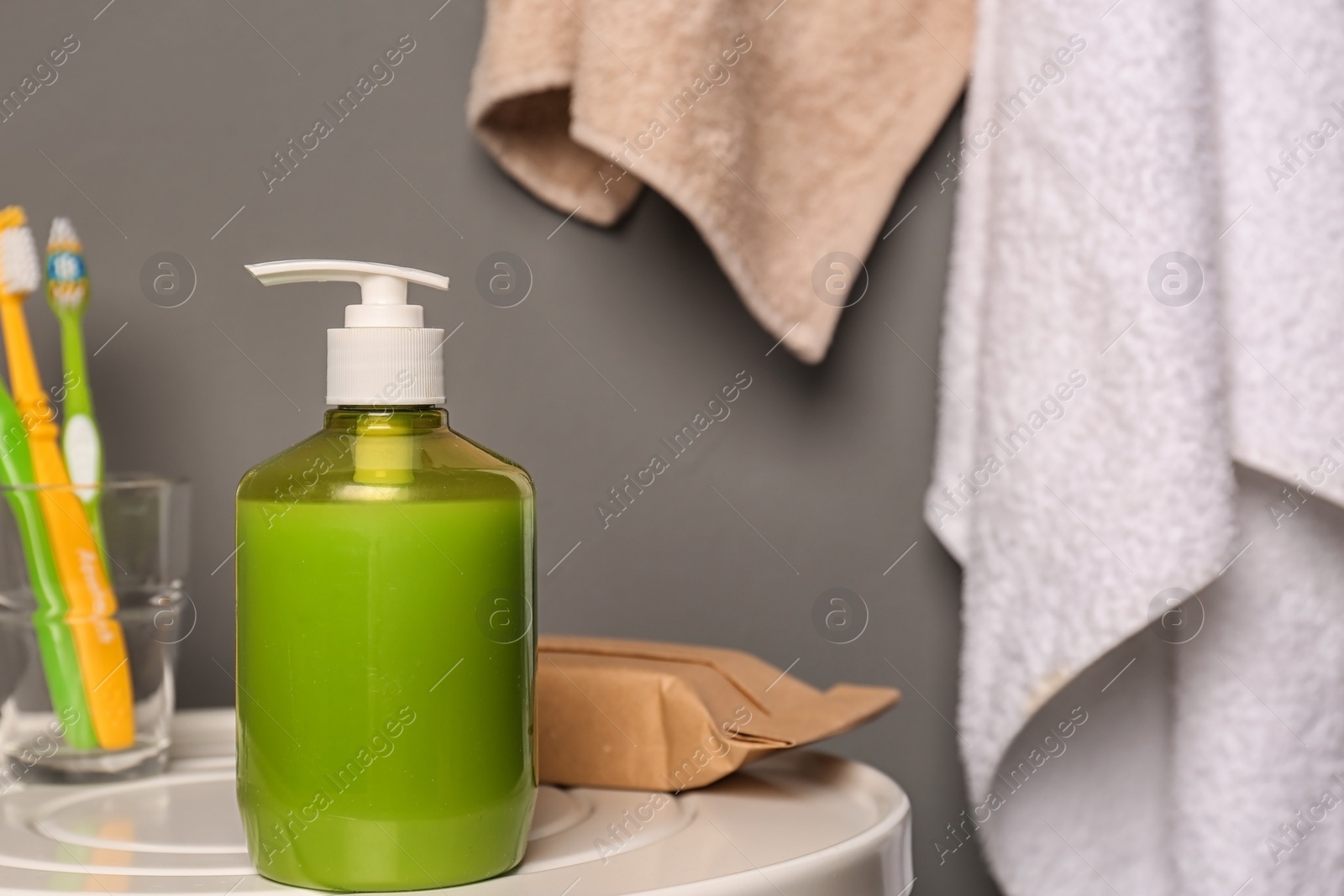 Photo of Glass with toothbrushes and bottle of liquid soap on table in bathroom