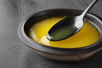 Photo of Spoon of clarified butter over bowl on black table, closeup